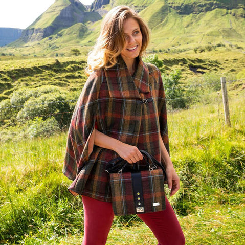 A multicolored tweed handbag with a black leather handle and metal twist clasp, sitting on a mossy surface.
