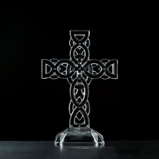 A clear glass Celtic cross ornament with intricate knot detailing, displayed against a black background.