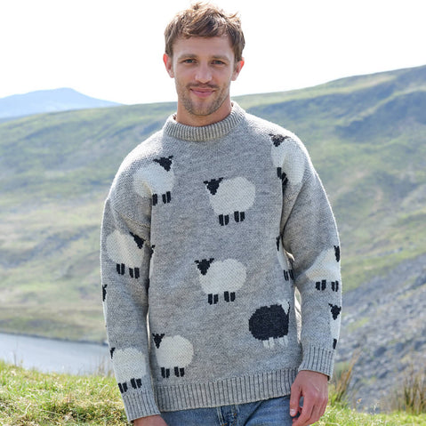 Man wearing a gray sweater with sheep pattern standing in a scenic outdoor setting.