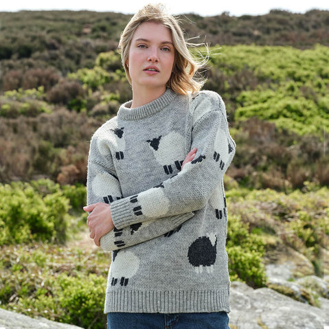 Woman wearing a gray sweater with white and black sheep patterns in a natural setting