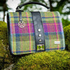 A multicolored tweed handbag with a black leather handle and metal twist clasp, sitting on a mossy surface.