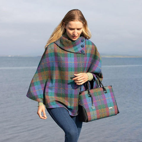 A handbag with a tweed body and vegan leather details, placed on a stone surface with foliage in the background.