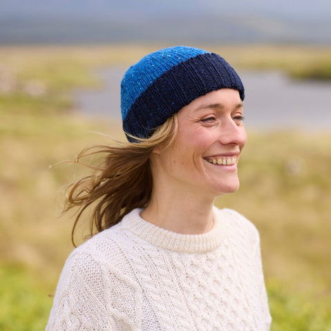 A woman wearing a blue wool hat with a darker brim, standing in a field.