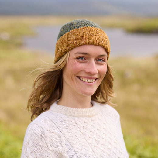 A woman wearing a beige wool hat with a darker brim, standing in a field.