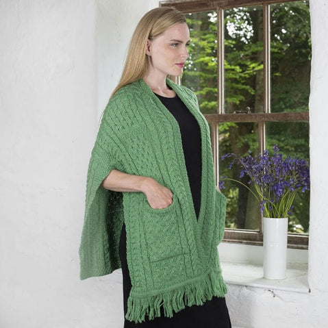 green merino wool pocket shawl with fringe trim, worn belted over a black dress beside a window.