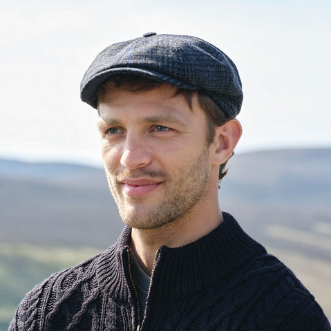 Man wearing a navy Irish flat cap and sweater with a blurred natural background