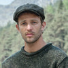 Man wearing a green knitted sweater and an Irish tweed flat cap with a mountainous background