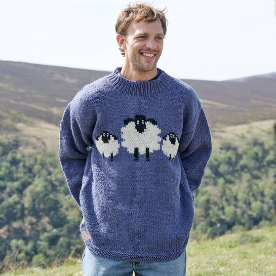 Man wearing a blue sweater with sheep designs in a mountainous landscape