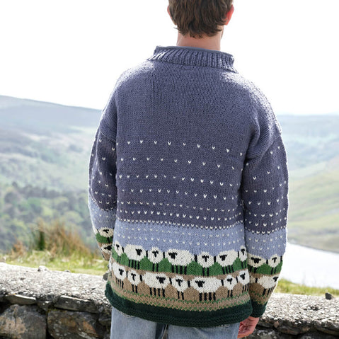 Person wearing a blue sweater with sheep pattern standing against a scenic mountain backdrop