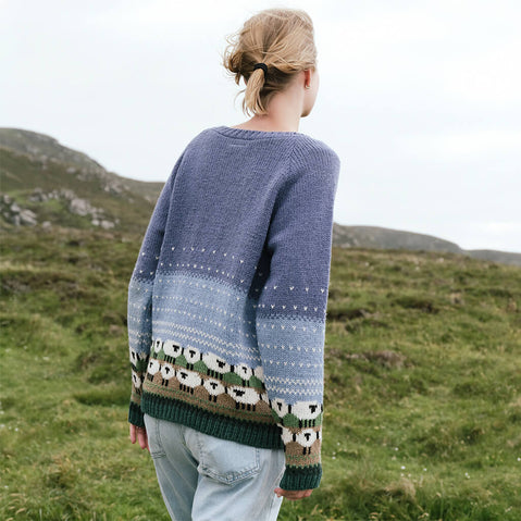 Back view of the Women's Button Front Hand Knit Sheep Cardigan, featuring a handcrafted blue ombré knit design and signature sheep motif detailing along the hem, inspired by traditional Irish knitwear and rural heritage.