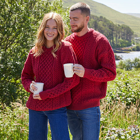 Couple wearing matching red cable knit Aran sweaters, ideal as authentic Irish heritage gifts for anniversaries or holidays.