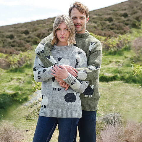 A couple wearing matching grey and green sheep pattern Irish wool sweaters from our signature sheep knitwear collection.