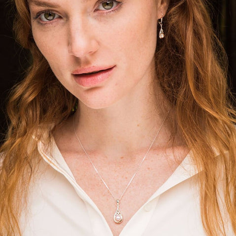 Silver Trinity Knot pearl pendant and matching drop earrings worn by an irish woman with a white collared shirt.