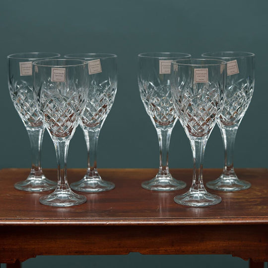 A set of six clear crystal wine glasses with a geometric pattern, displayed on a wooden surface against a teal background.