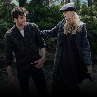 Two people standing outdoors with greenery in the background wearing authentic irish clothing