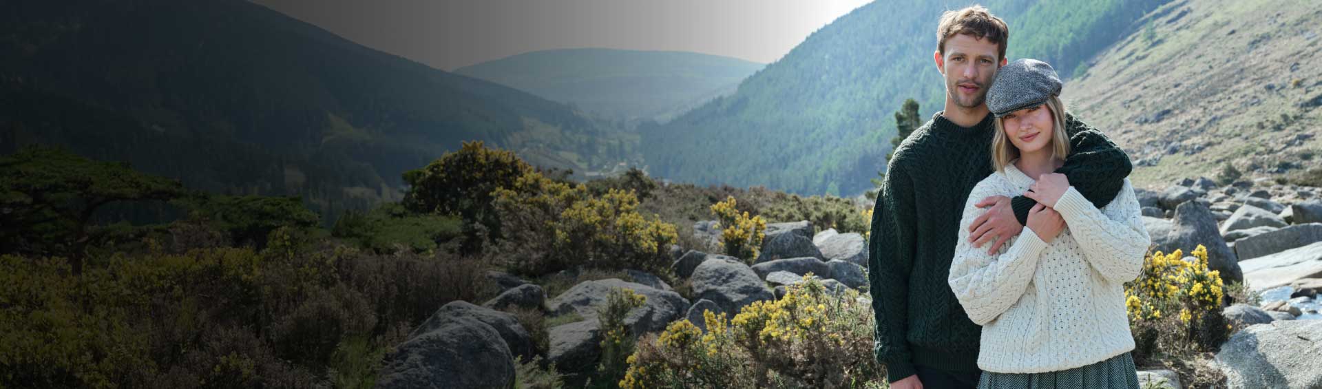 Two people standing in a scenic outdoor setting with mountains and rocks.