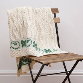 A beige baby blanket with green shamrock and sheep patterns draped over a wooden chair.