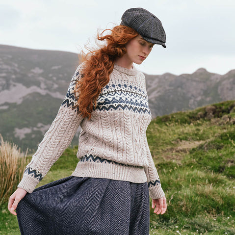 Women's Fair Isle Cable Knit Sweater in oatmeal, crafted with traditional Fair Isle motifs and authentic cable knit textures, showcased from a side view against a scenic Irish mountain landscape.