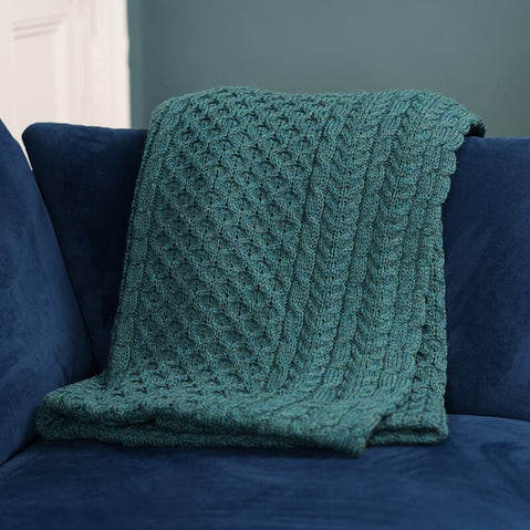 Teal cable-knit throw blanket with diamond lattice pattern draped over a navy blue couch, styled against a teal accent wall and white trim—perfect for cozy, modern living room décor and textile inspiration.