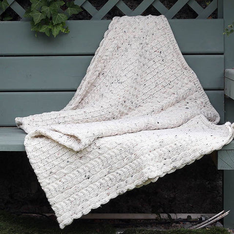Traditional Aran Honeycomb Wool Throw in oatmeal flecked yarn draped on a wooden garden bench