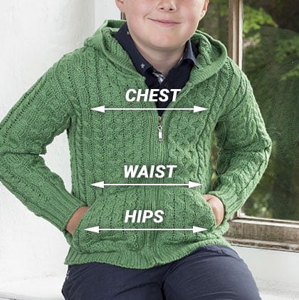 A boy wearing a green, knitted aran hoodie is seated near a window. The image includes measurements labeled as