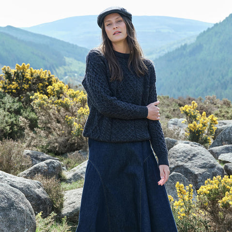 Woman in a charcoal knitted outfit standing in a mountainous landscape with yellow flowers.