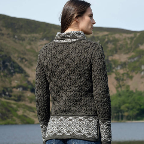 Woman wearing a dark green Aran sweater with white patterns standing in a scenic outdoor setting.