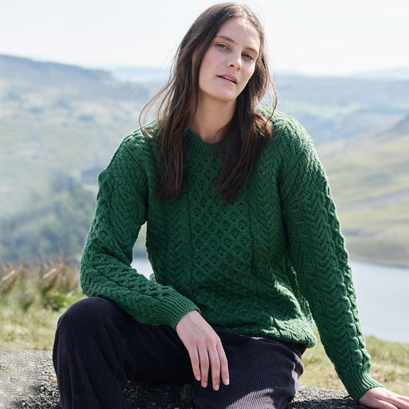 Woman wearing a green Aran sweater sitting outdoors with a scenic background
