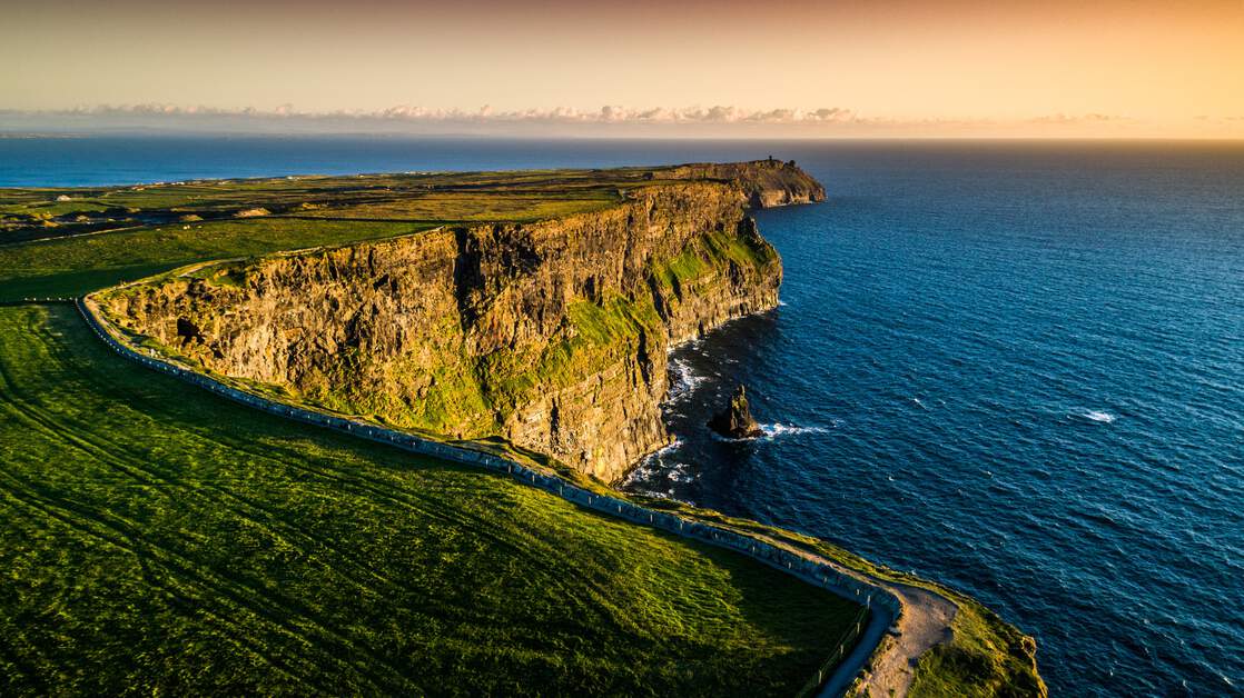 Cliffs of Moher, County Clare. Aerial view of a rugged coastline at sunset, featuring steep cliffs and a winding road along the edge.