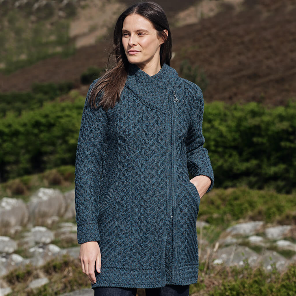Woman wearing a peacock knitted coat standing outdoors with a natural background