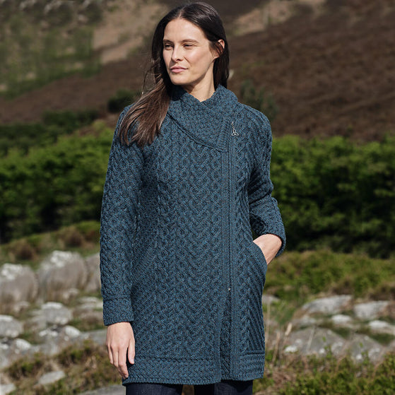 Woman wearing a peacock knitted coat standing outdoors with a natural background