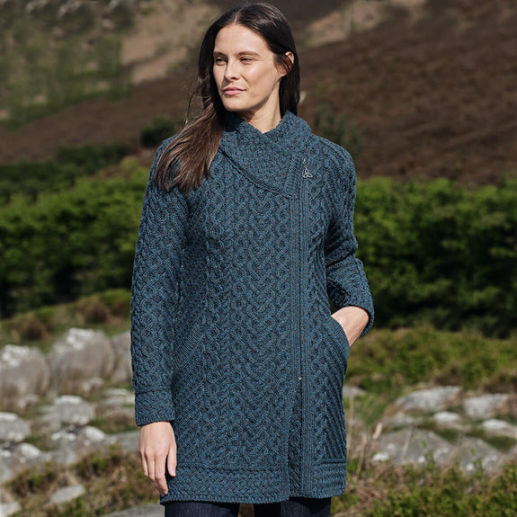Woman wearing a peacock knitted coat standing outdoors with a natural background