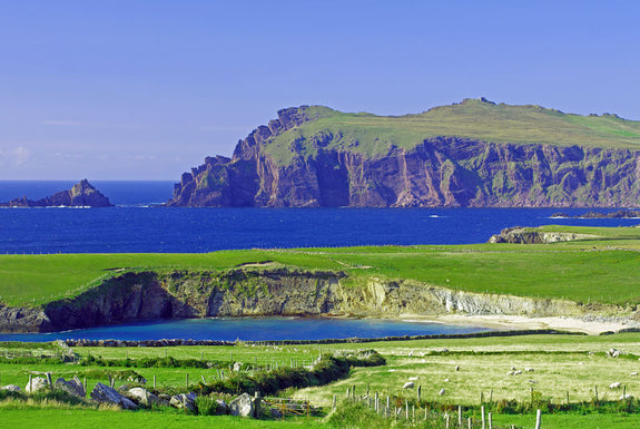 A panoramic view of an Irish coastal landscape featuring a rugged cliffside and the deep blue ocean.