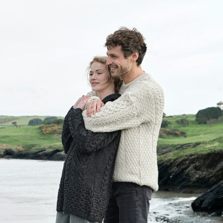 Couple embracing on a beach with a scenic background wearing traditional aran sweaters
