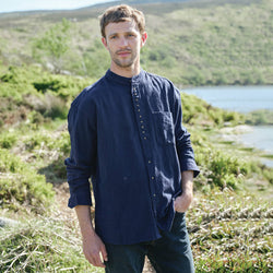 Man wearing a navy blue shirt standing in a natural landscape with a lake and hills.