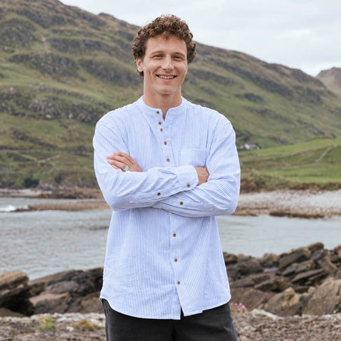 Image featuring the Blue Stripe Grandad Shirt, crafted with a traditional Irish grandad collar, classic blue and white stripe design, button-front placket, and relaxed fit, showcasing timeless Irish style against a scenic coastal landscape.