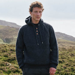 Image featuring the Men's Ribbed Hooded Sweater in Atlantic Marl, crafted with a rich ribbed knit texture, button-detail placket, and comfortable hood, inspired by traditional Irish knitwear and showcased in a scenic countryside setting.