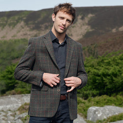Man wearing a tweed jacket outdoors with mountains in the background