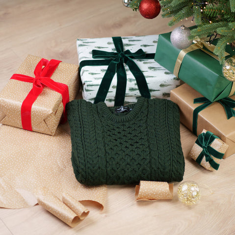 Green knitted aran sweater on a wooden floor with Christmas presents and decorations.