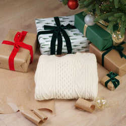 Cream-colored hand-knit Aran sweater with traditional cable patterns, photographed against a festive Christmas background with holiday decorations.
