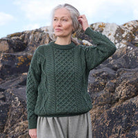 Woman wearing a green knitted Aran sweater standing against a rocky background