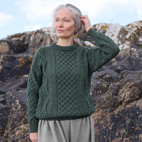 Woman wearing a green knitted Aran sweater standing against a rocky background