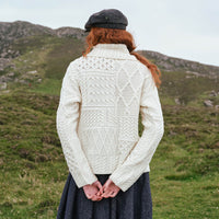 Back view of the Women's One Button Aran Cardigan in cream, crafted with authentic Irish Aran cable knit patterns and a statement shawl collar, showcasing the intricate heritage-inspired knit design in a scenic countryside setting.
