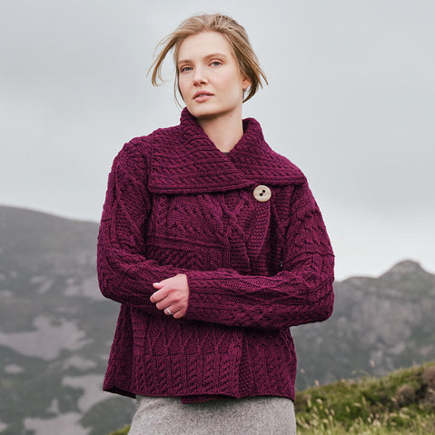 Image featuring the Women's One Button Aran Cardigan in damson, crafted with authentic Irish Aran cable knit patterns, a statement shawl collar, and classic one-button closure, showcasing timeless Irish craftsmanship in a scenic countryside setting.