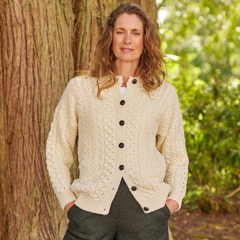 Woman wearing a cream-Womens Traditional Cable Knit Aran Cardigan standing next to a tree