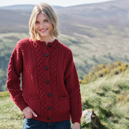 Woman wearing a red knitted cardigan standing in a scenic outdoor setting with mountains in the background.