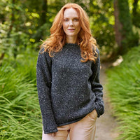 Woman wearing a charcoal Women's Traditional Fisherman Irish Wool Sweater standing in a forest