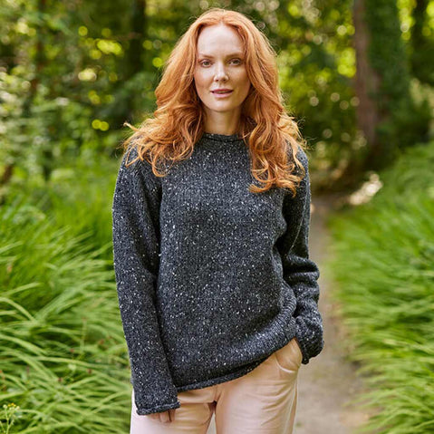 Woman wearing a charcoal Women's Traditional Fisherman Irish Wool Sweater standing in a forest