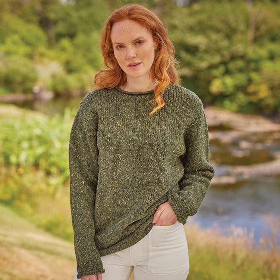 Woman wearing a green Women's Traditional Fisherman Irish Wool Sweater standing outdoors by a stream.
