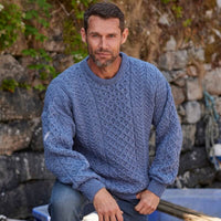 Man wearing a blue knitted sweater sitting against a stone wall.